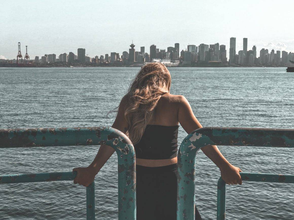Girl standing next to the ocean with the view of Vancouver city.